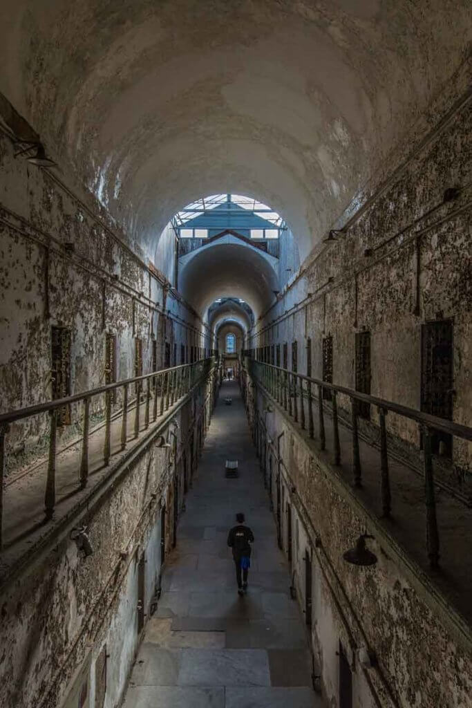 Aerial view of an abandoned prison with a person walking down the hallway.